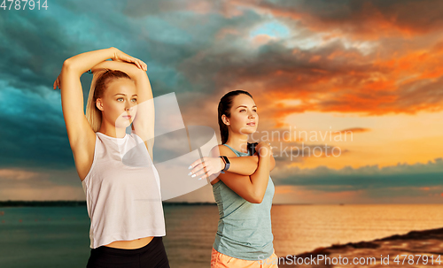 Image of women with fitness trackers stretching over sea