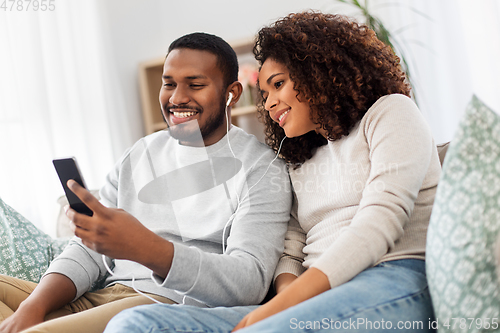 Image of happy couple with smartphone and earphones at home