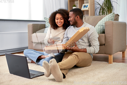 Image of happy african american couple eating pizza at home