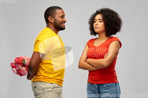 Image of man hiding bunch of flowers behind back from woman