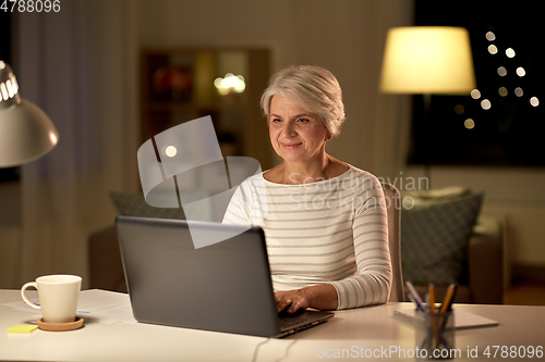 Image of happy senior woman with laptop at home in evening