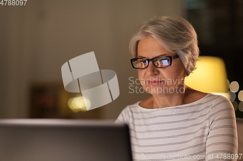 Image of happy senior woman with laptop at home in evening