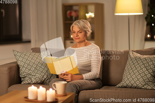 Image of happy senior woman reading book at home in evening