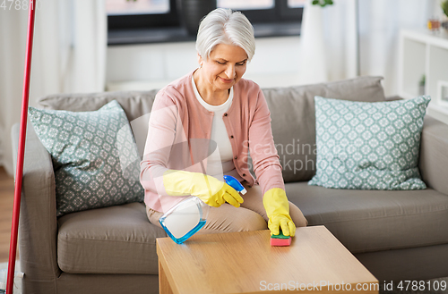 Image of senior woman with detergent cleaning table at home