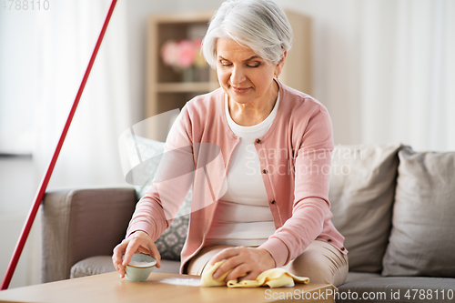 Image of senior woman cleaning table with soda at home