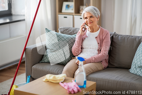 Image of old woman calling on cellphone after cleaning home