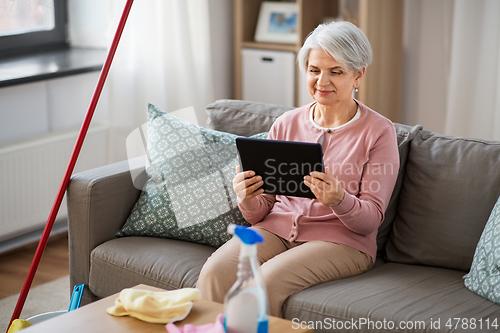 Image of senior woman using tablet pc after cleaning home