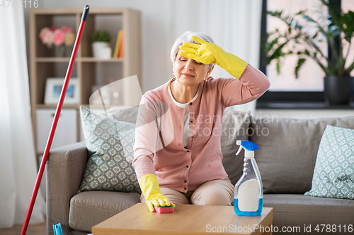 Image of tired senior woman cleaning table at home