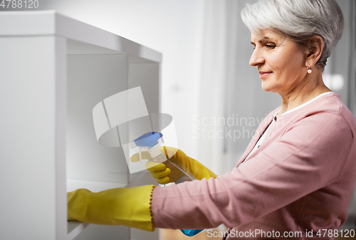 Image of senior woman cleaning rack with detergent at home