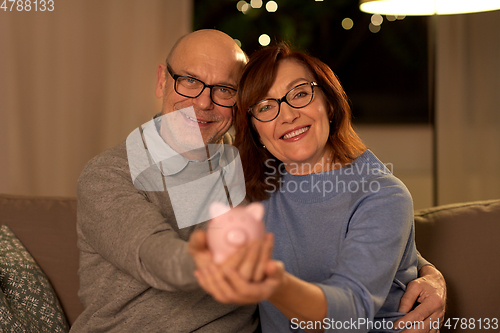 Image of happy senior couple with piggy bank at home