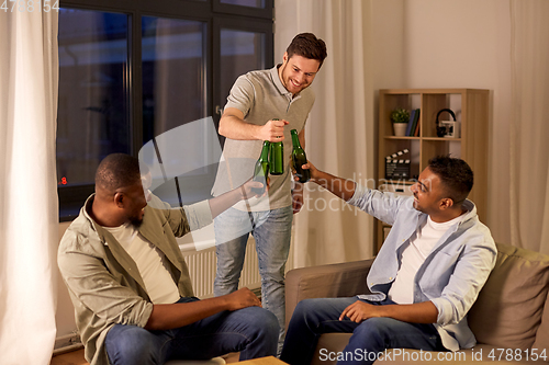 Image of happy male friends drinking beer at home at night