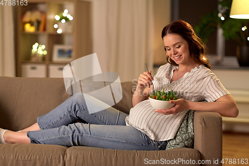 Image of happy smiling pregnant woman eating salad at home