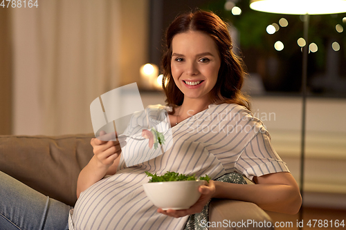 Image of happy smiling pregnant woman eating salad at home