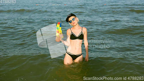 Image of Happy young woman in a cap with the word queen playing with water gun. Film effect