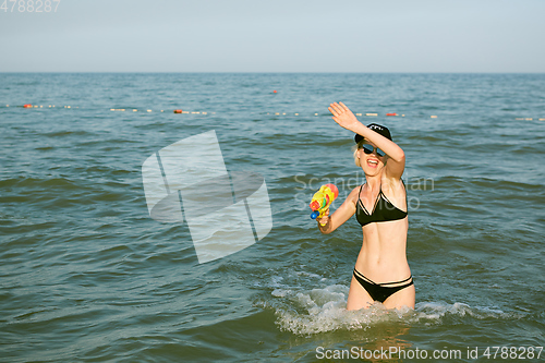Image of Happy young woman in a cap with the word queen playing with water gun. Film effect
