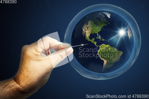 Image of Planet earth in a soap bubble and a hand with a needle that burs