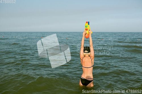 Image of Happy young woman in a cap with the word queen playing with water gun. Film effect