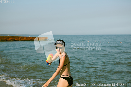 Image of Happy young woman in a cap with the word queen playing with water gun. Film effect