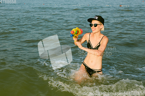 Image of Happy young woman in a cap with the word queen playing with water gun. Film effect