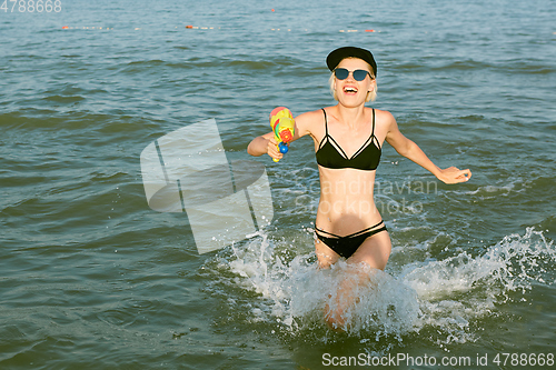 Image of Happy young woman in a cap with the word queen playing with water gun. Film effect