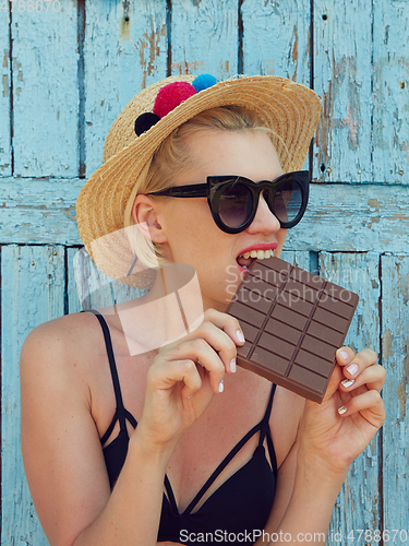 Image of Young attractive woman in sunglasses and in straw hat eating chocolate on a blue background. Film efect