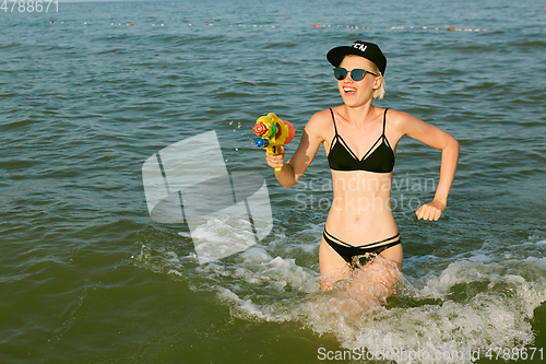 Image of Happy young woman in a cap with the word queen playing with water gun. Film effect