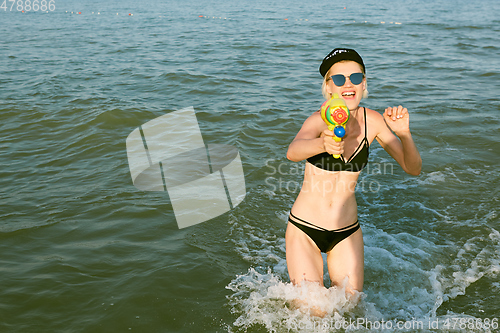 Image of Happy young woman in a cap with the word queen playing with water gun. Film effect