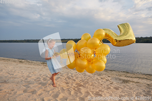 Image of Little girl with many golden balloons on the beach at sunset