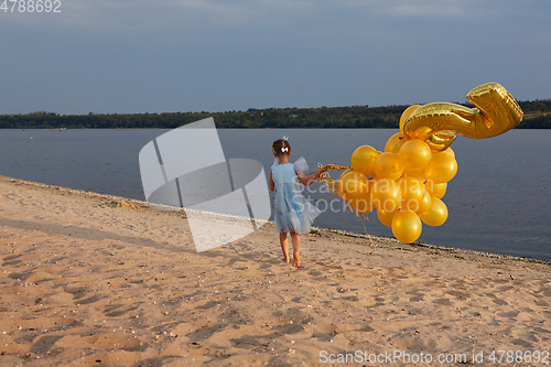 Image of Little girl with many golden balloons on the beach at sunset