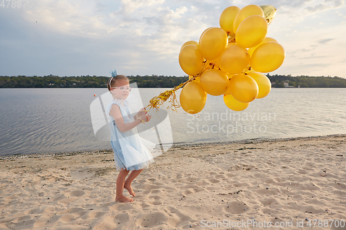 Image of Little girl with many golden balloons on the beach at sunset