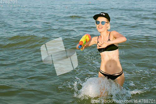 Image of Happy young woman in a cap with the word queen playing with water gun. Film effect