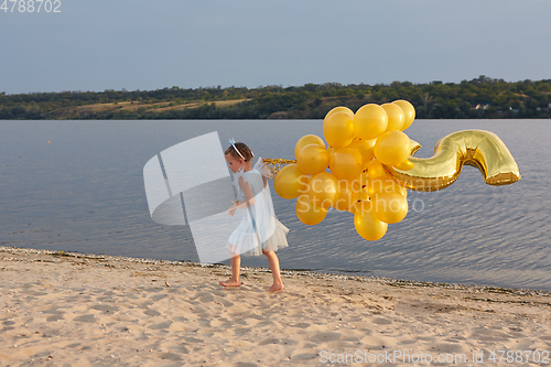 Image of Little girl with many golden balloons on the beach at sunset