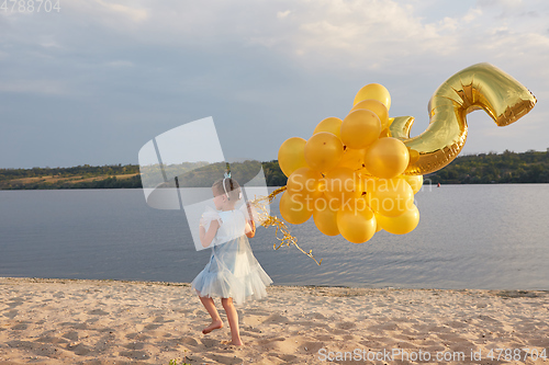 Image of Little girl with many golden balloons on the beach at sunset