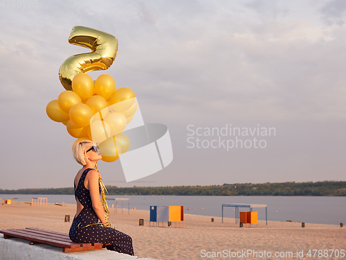 Image of Young woman with many golden balloons.