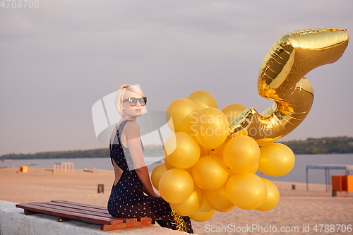 Image of Young woman with many golden balloons.