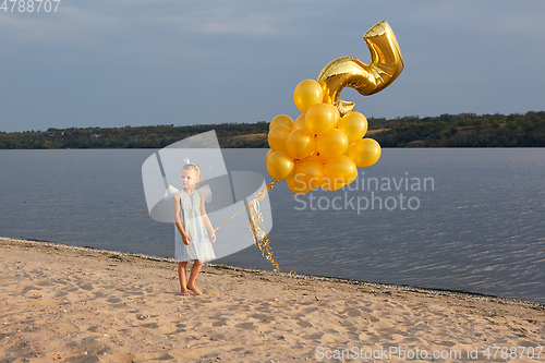 Image of Little girl with many golden balloons on the beach at sunset