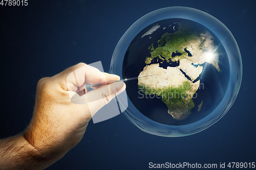 Image of Planet earth in a soap bubble and a hand with a needle that burs