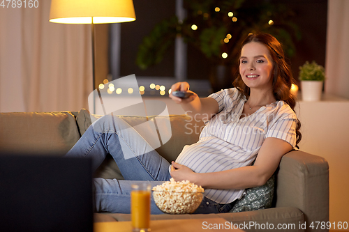 Image of pregnant woman with remote control watching tv