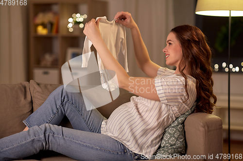 Image of happy pregnant woman with baby bodysuit at home