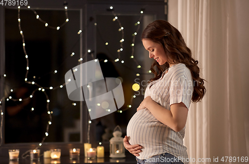 Image of happy pregnant woman looking out window at home