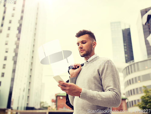 Image of young man with bag texting on smartphone in city