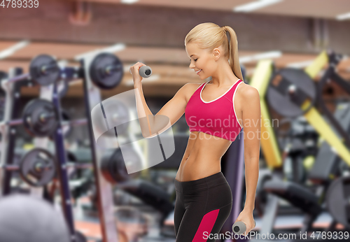 Image of happy young woman with dumbbells exercising in gym