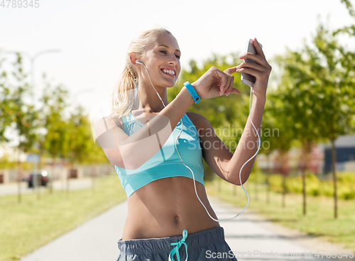 Image of happy woman with smartphone and earphones outdoors