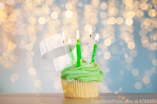 Image of green cupcake with six burning candles on table