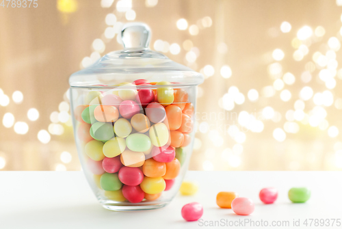 Image of glass jar with candy drops over lights background