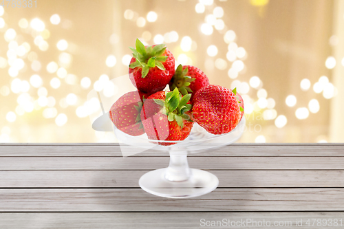 Image of strawberries on glass stand over lights background