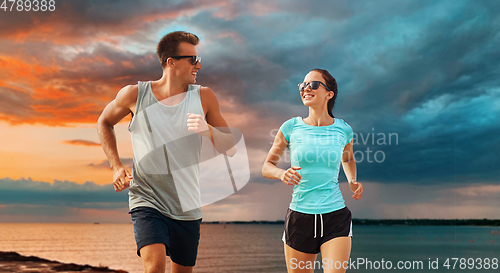 Image of couple in sports clothes running along on beach