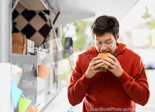 Image of hungry young man eating hamburger at food truck