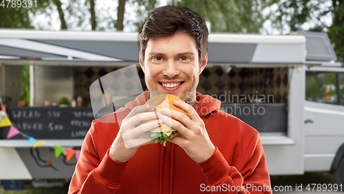 Image of happy young man eating hamburger at food truck