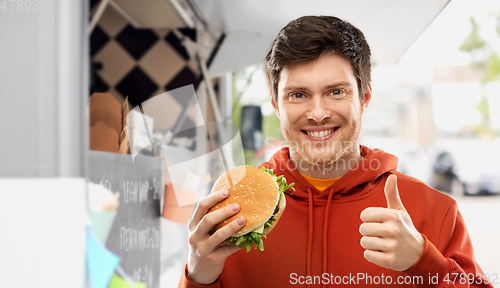 Image of happy young man with hamburger showing thumbs up